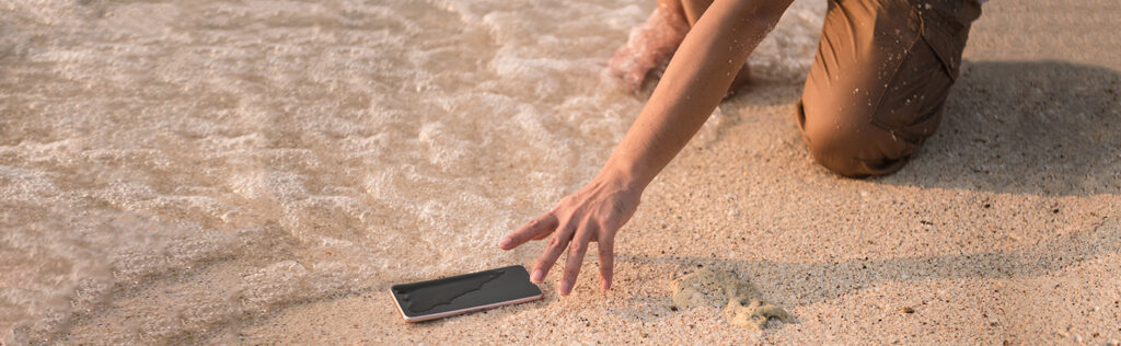person reaching for phone that got wet at the beach from ocean waves
