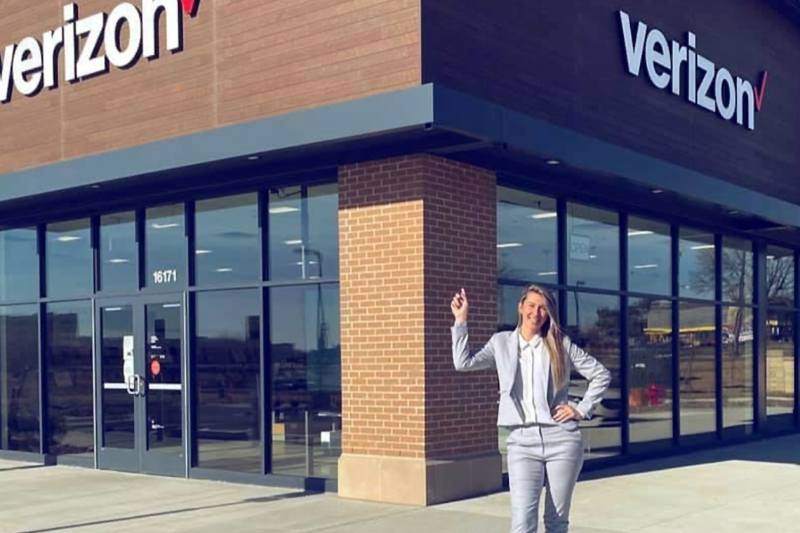 Cellular Sales team member standing in front of store pointing to Verizon logo