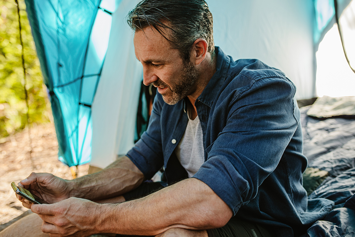 Man sitting in tent while streaming a show on a 5g smartphone