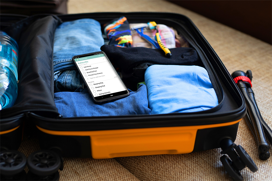 Smartphone sitting on top of open travel case full of clothes