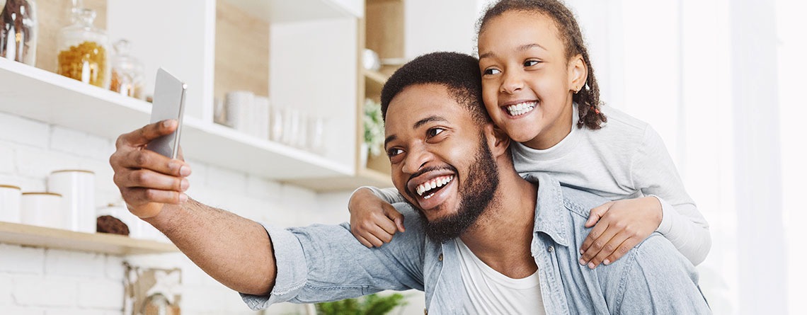 Daughter on Dad's back taking selfie with smartphone