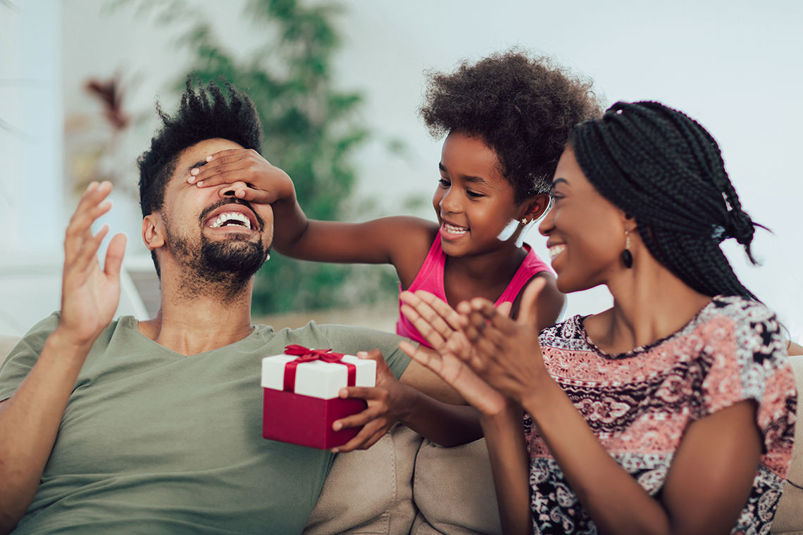 Family sitting on couch surprising Dad with Father's Day 2021 gifts