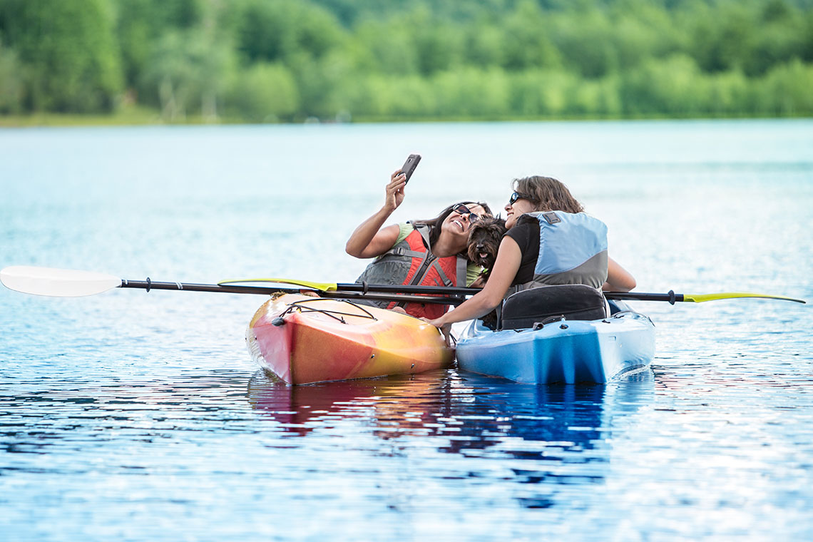 2 woman taking selfie on water in kayaks