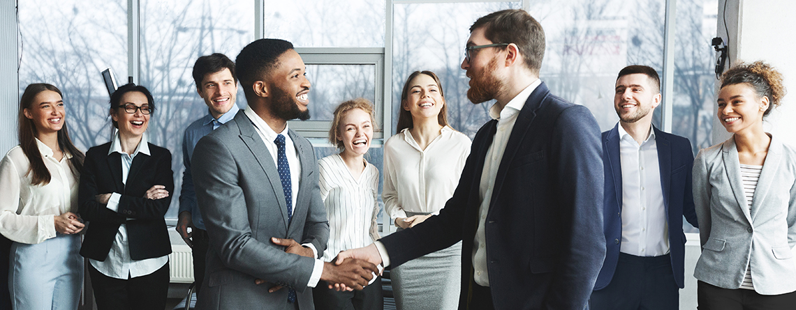 two men shaking hands while group of professionals congratulating in background