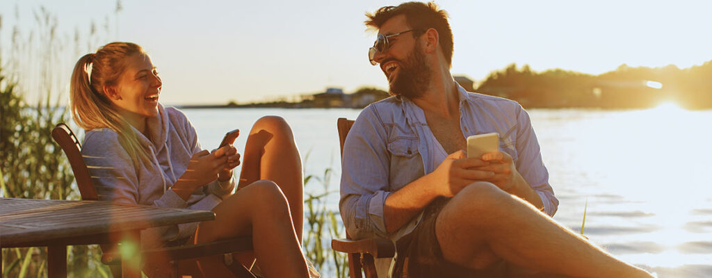 couple sitting on dock at lake with smartphones