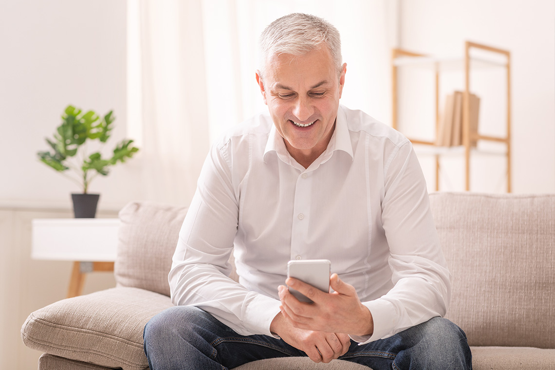senior man holding smartphone sitting on couch