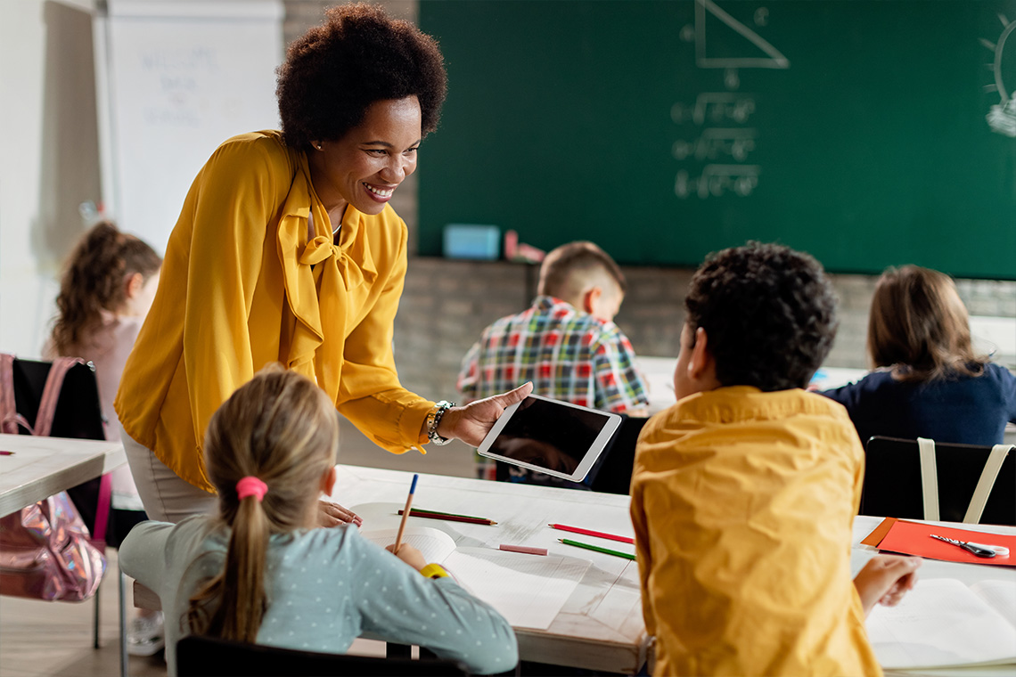 teacher helping students while holding a tablet - blog post