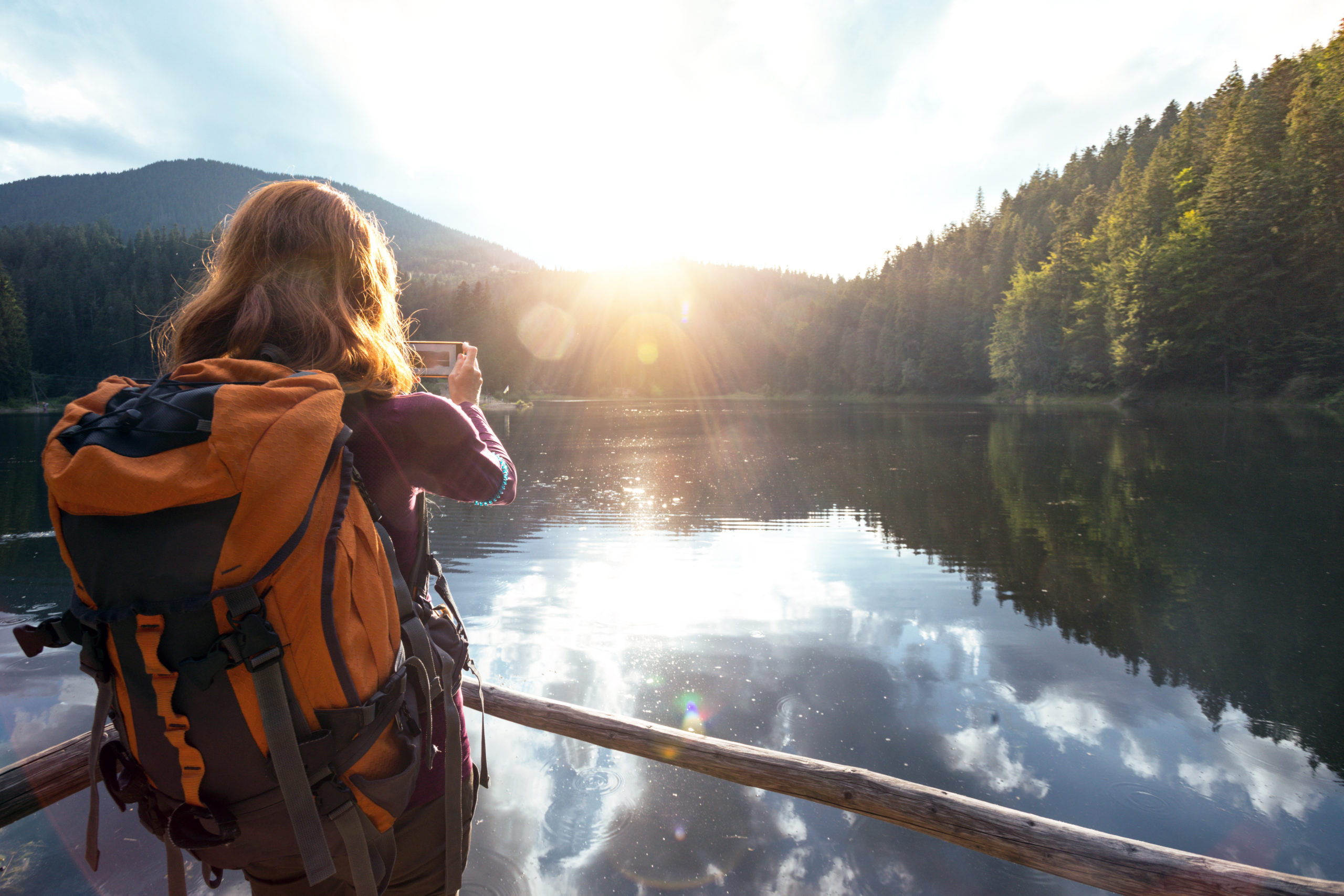 woman with backpack on taking picture of lake