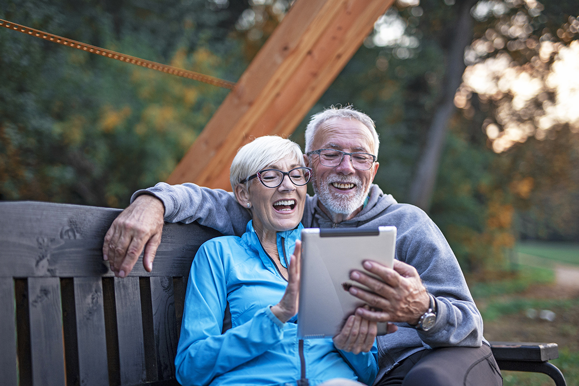 senior couple watching videos and smiling on apple ipad outside