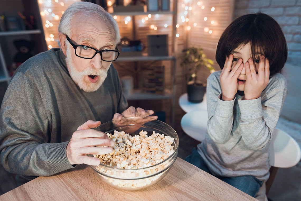 grandfather and grandson watching scary movie with popcorn