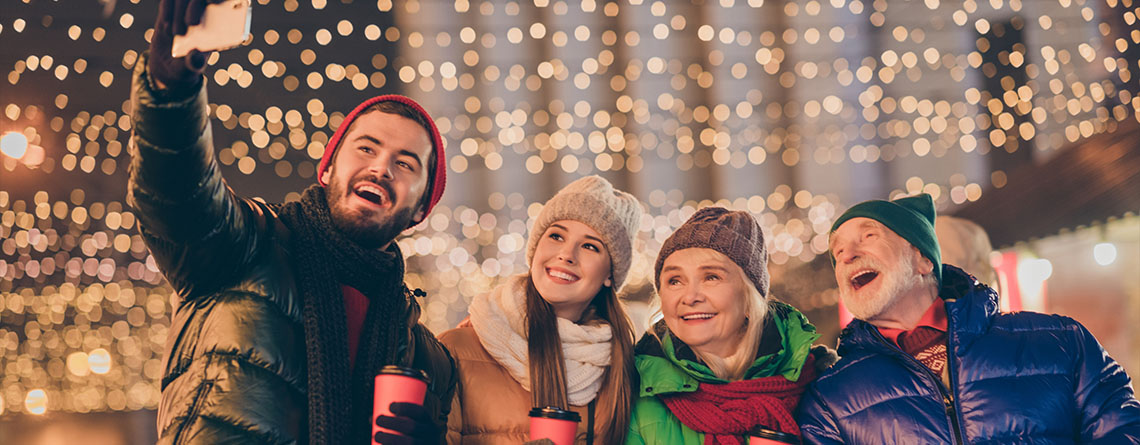 family taking selfie outside in front of christmas lit up with lights