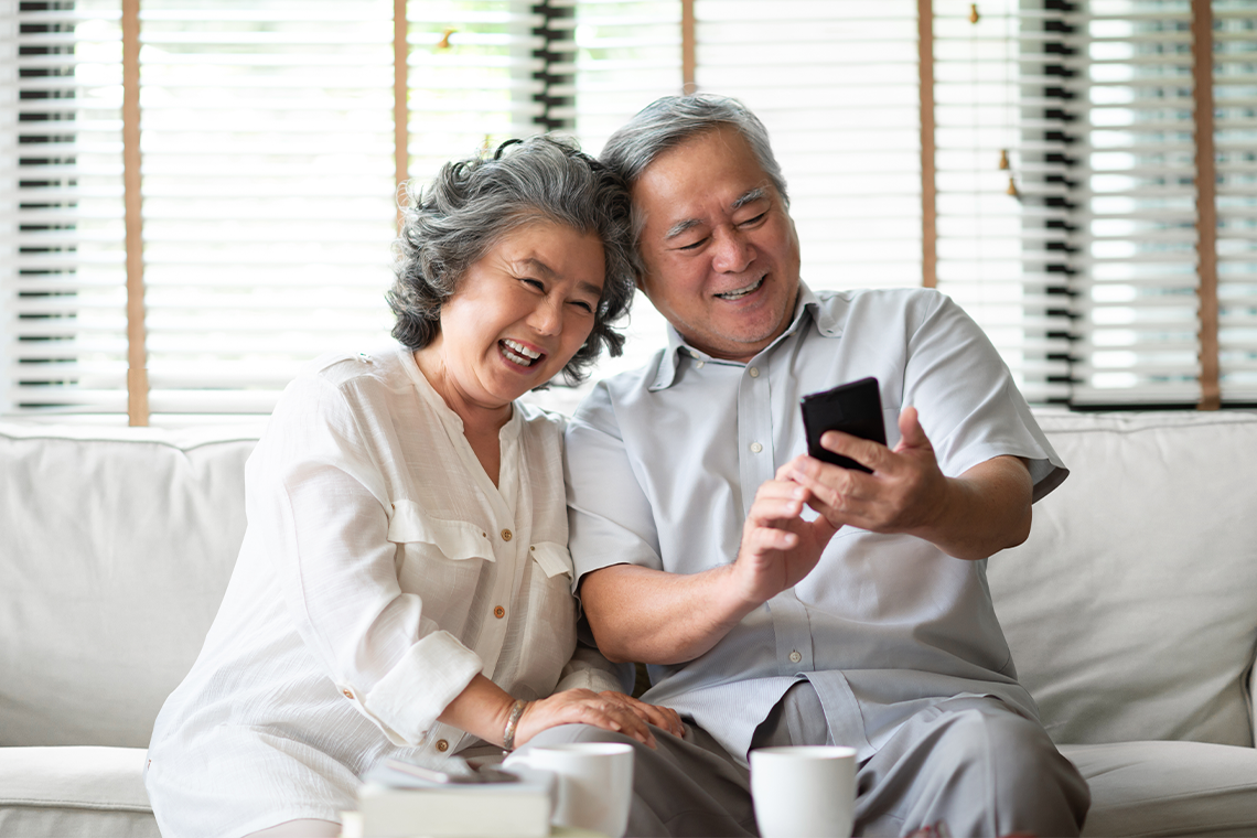 senior couple laughing while looking at smartphone