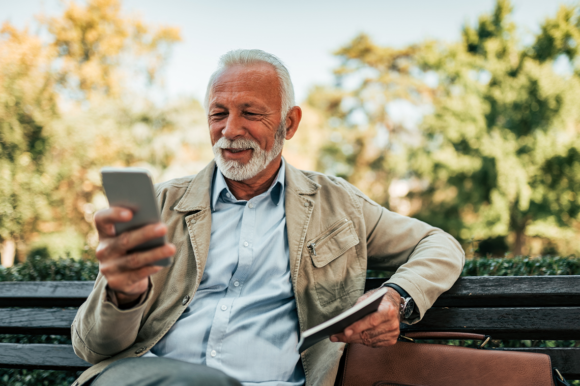 senior man looking at smartphone on bench