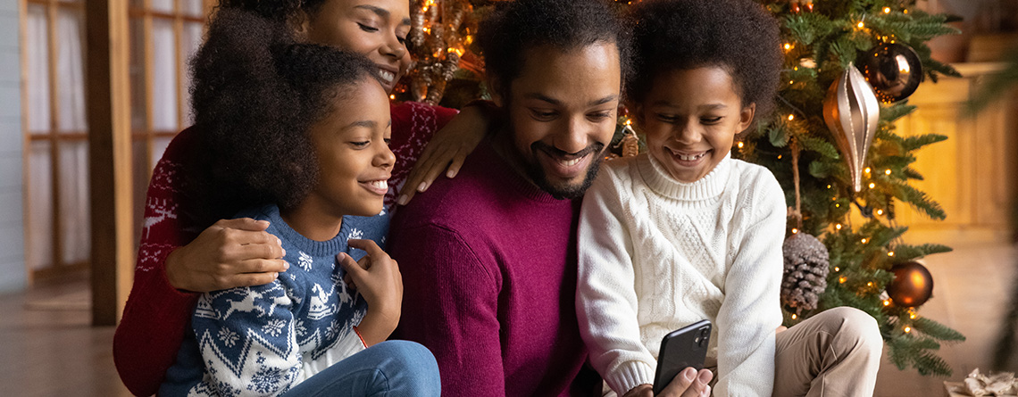 family watching video on smartphone in front of christmas tree