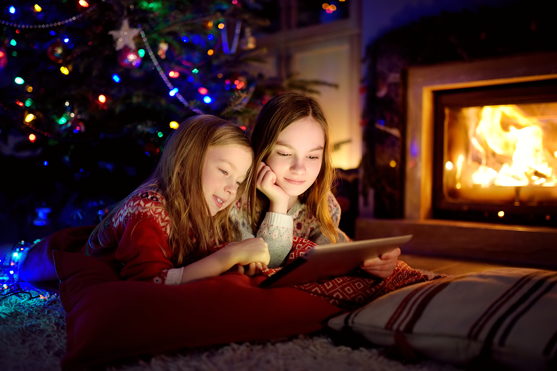 two sisters looking at iPad in front of christmas tree