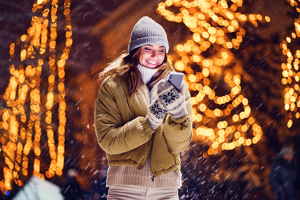 woman smiling at smartphone outside while snowing