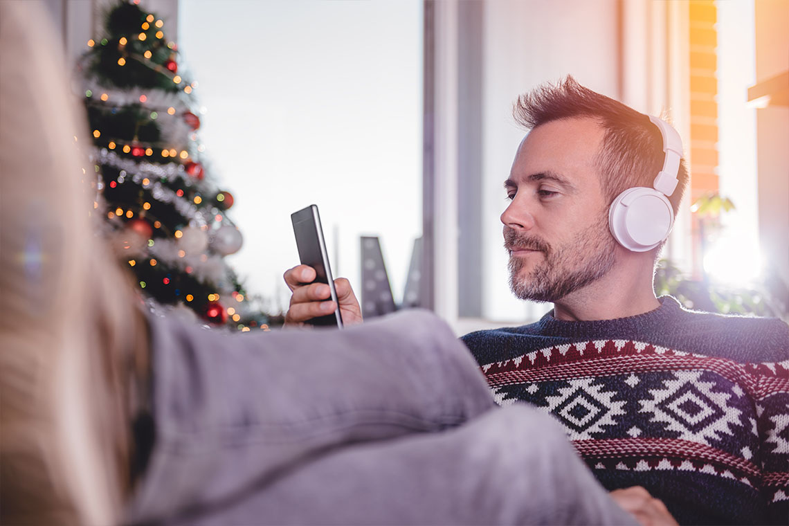 man with headphones listing to holiday playlist on smartphone