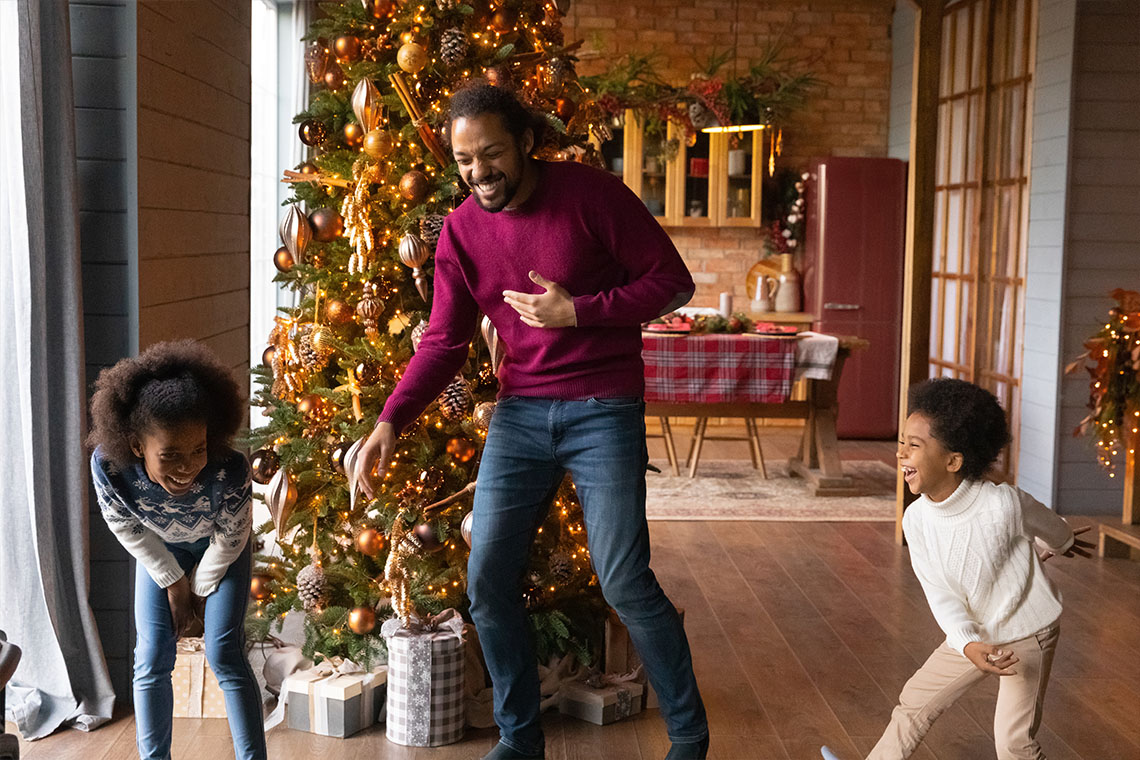 family dancing in front of christmas tree listing to holiday music playlist