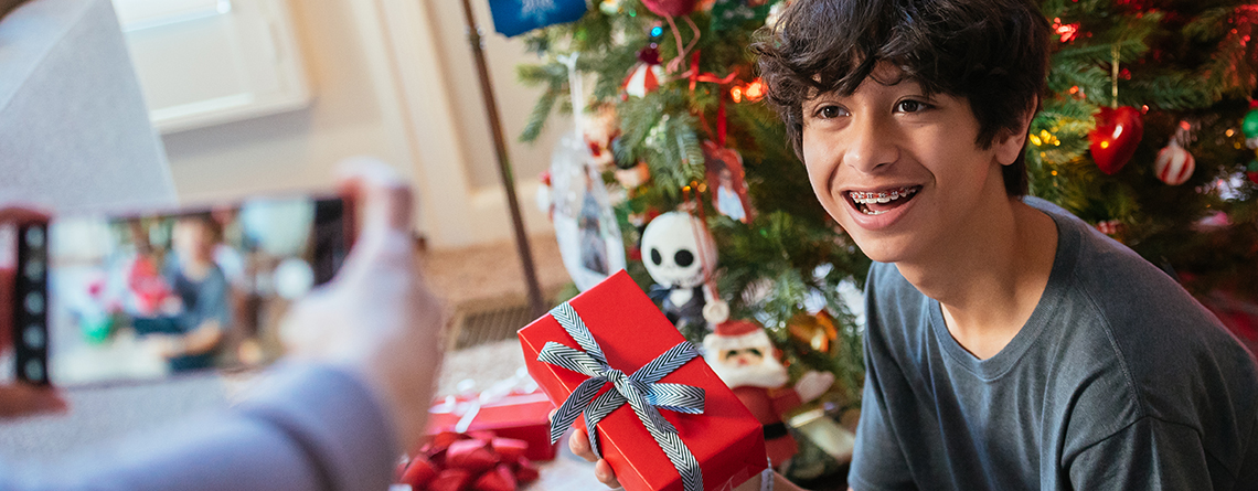 Teenager holding up Christmas gift while mother takes photo on smartphone