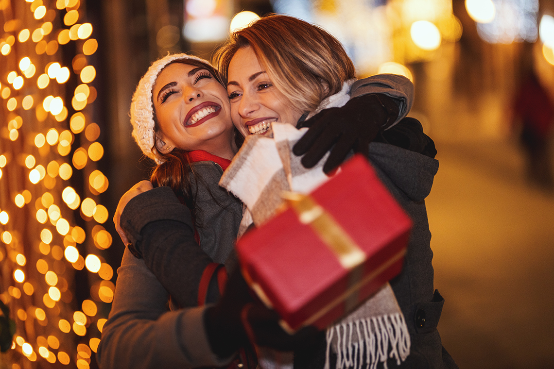 best friends hugging outside in winter with christmas lights in background