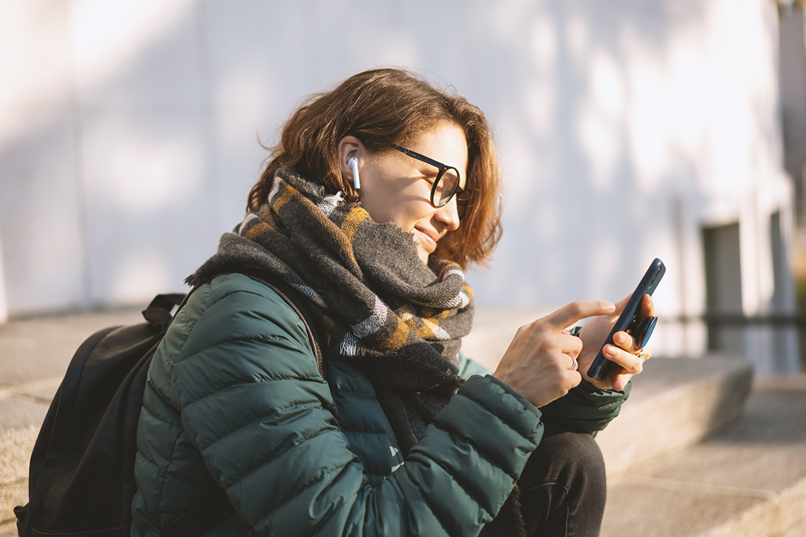 Young woman with wireless headphones and mobile device listening to music outdoor in city