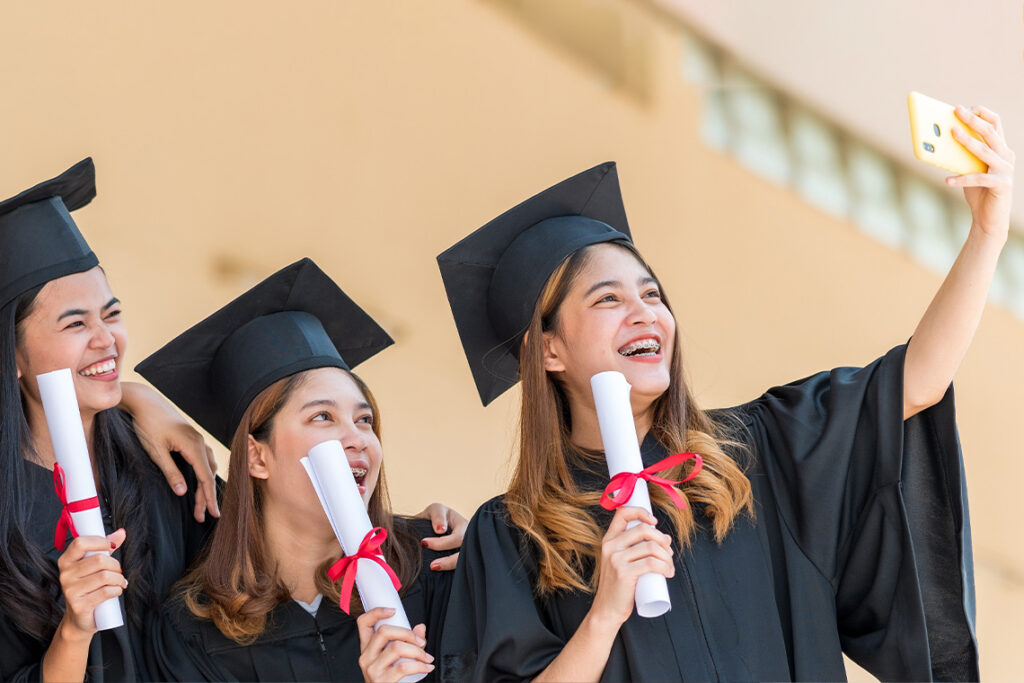 Three young women smile and pose in their graduation gowns, holding diplomas.