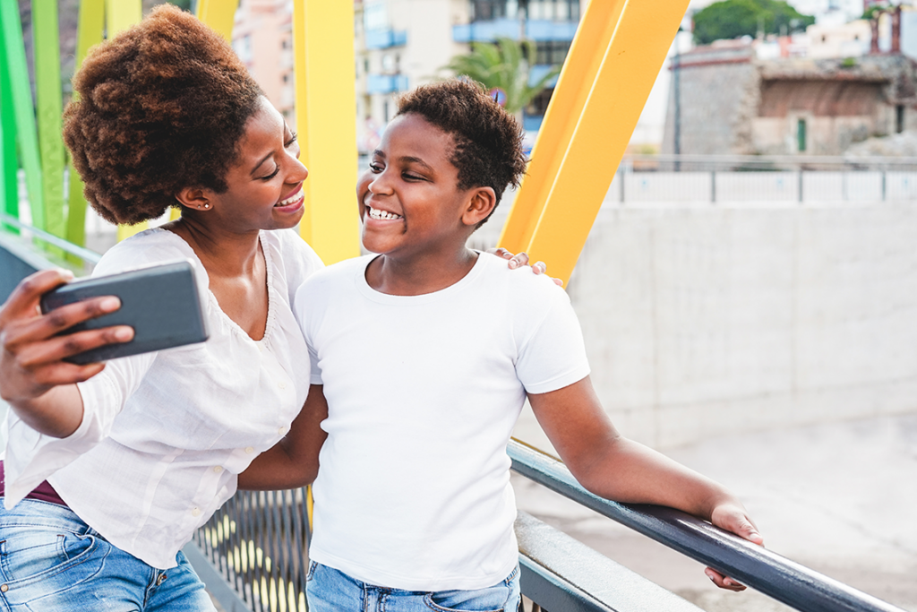 A woman and son in white tee-shirts smile at each other while posing for a selfie.