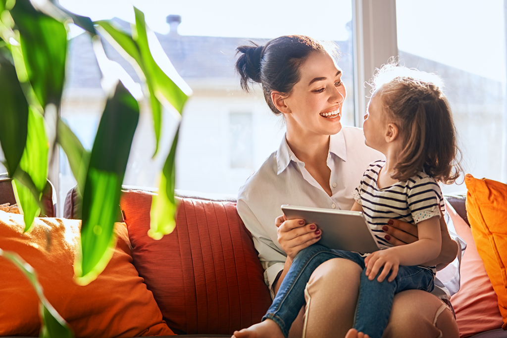A woman sits on an orange sofa smiling at a child, who is sitting on her lap.