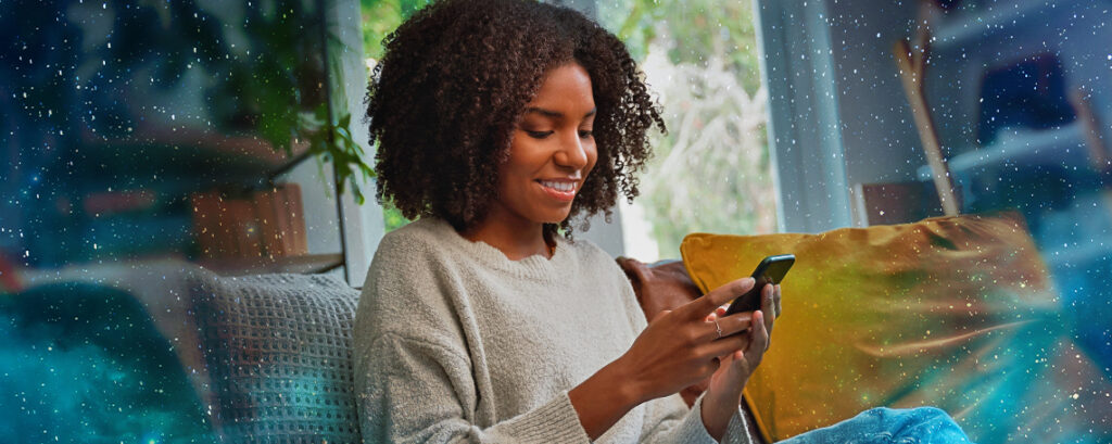 A young Black woman in a beige sweater sits on a couch, smiling down at her phone. She is surrounded by an overlay of stars.