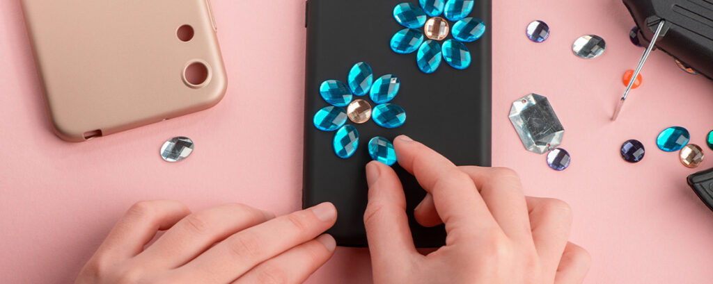 DIY phone case decorating. Blue gem stickers make up two flowers on a black phone case.