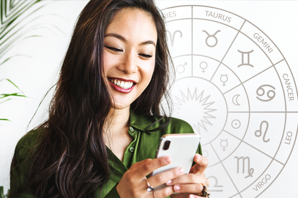 A young Asian woman in a green top holds a white smartphone. In the background is a round zodiac chart.
