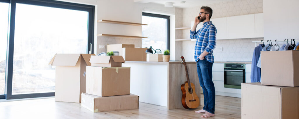 A man stands in a room, talking on the phone and surrounded by moving boxes.
