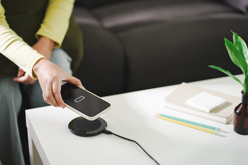 A person holds their low battery phone over a wireless charging pad.