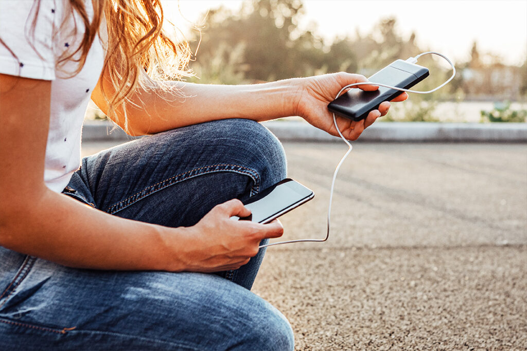 A person with long blonde hair, wearing a white teeshirt and jeans, is holding a smartphone in each hand.
