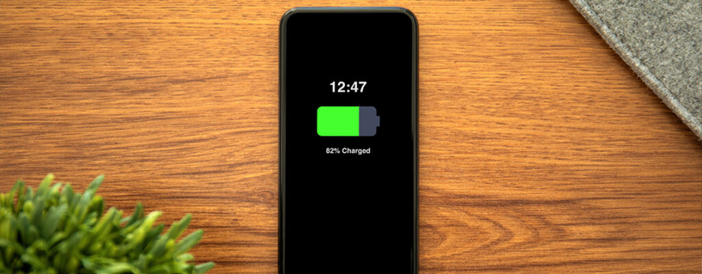 A phone sits on a desk, charging. The green battery icon on the screen reads, "82% charged."
