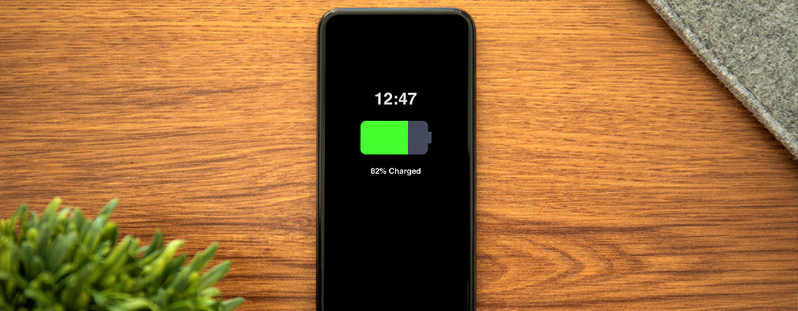 A phone sits on a desk, charging. The green battery icon on the screen reads, "82% charged."