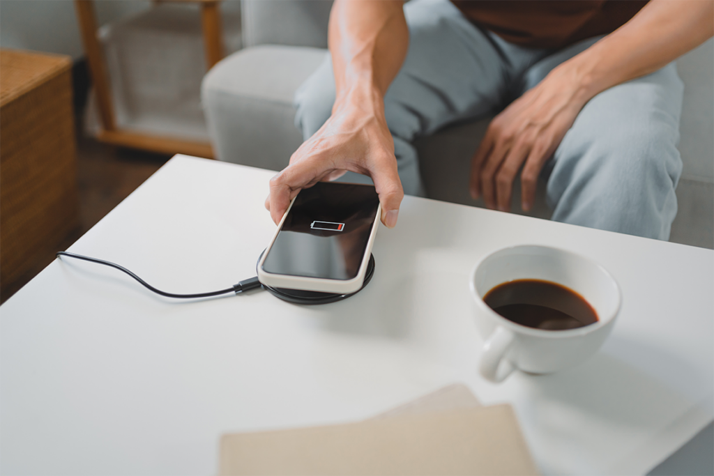 A sits at a coffee table, on which are a cup of coffee and a smartphone on a wireless charger.