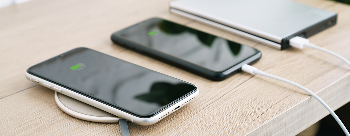 Two smartphones sit charging on a table, one wirelessly and the other with a portable charger.