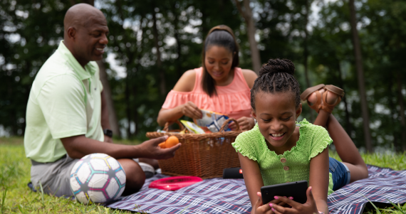 family having a picnic while daughter watches phone