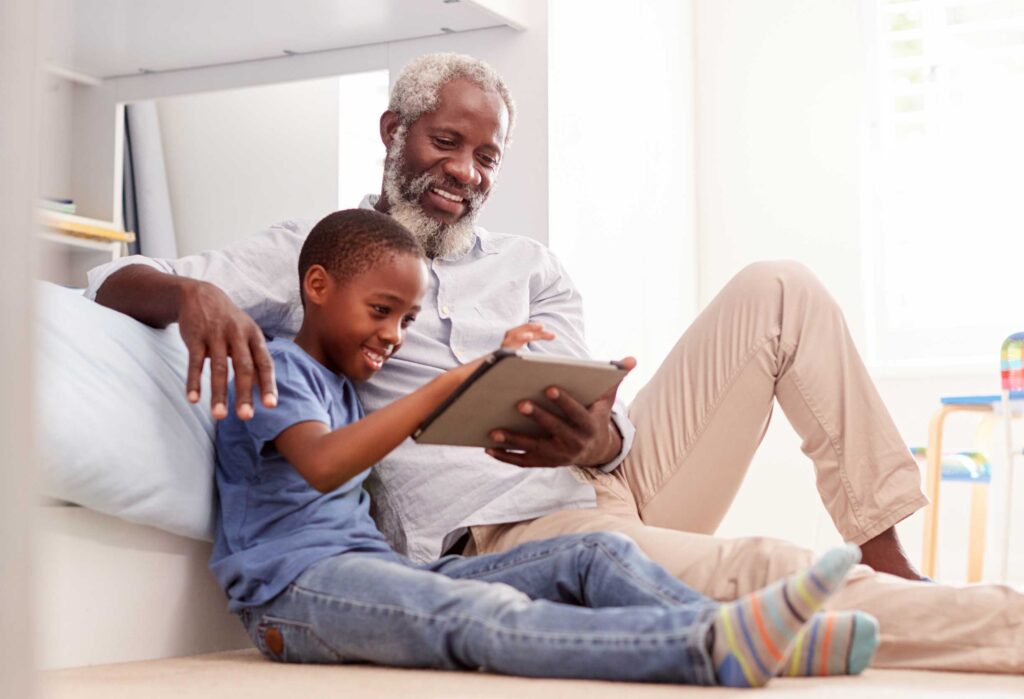 man sitting on floor with grandson using tablet