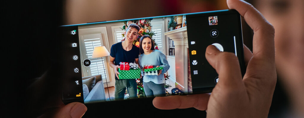 A hand holds a smartphone horizontally, on the screen is a photo of two teens holding gift wrapped presents.