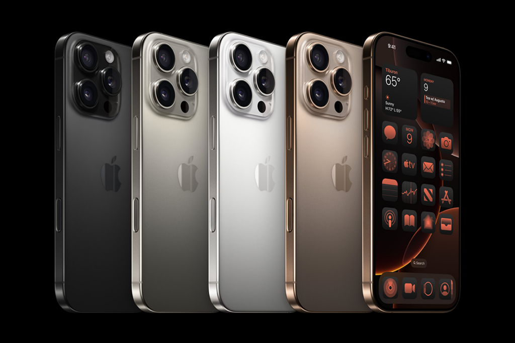 A lineup of Apple iPhone 16 Pro devices from left to right in Black Titanium, White Titanium, Natural Titanium, and Desert Titanium.